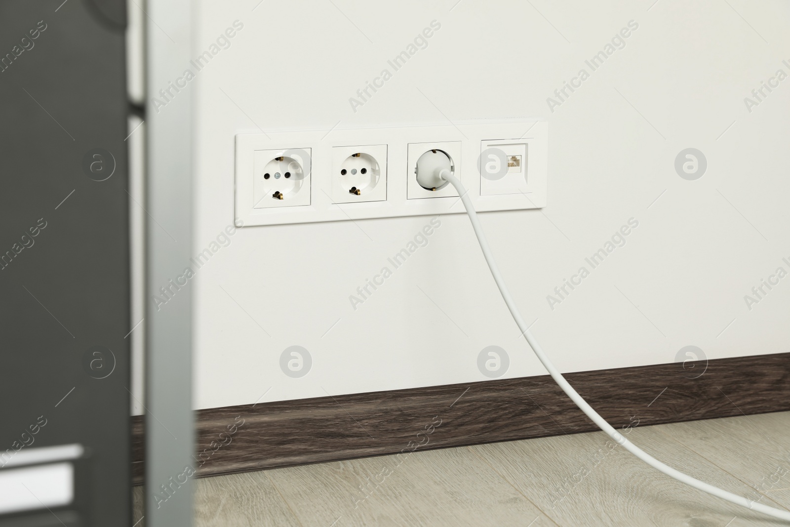 Photo of Power sockets with inserted plug on white wall indoors. Electrical supply