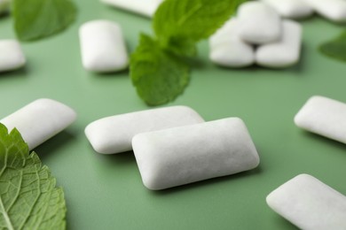 Photo of Tasty white chewing gums and mint leaves on light green background, closeup