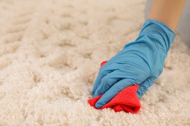 Photo of Woman in rubber gloves cleaning carpet with rag, closeup. Space for text