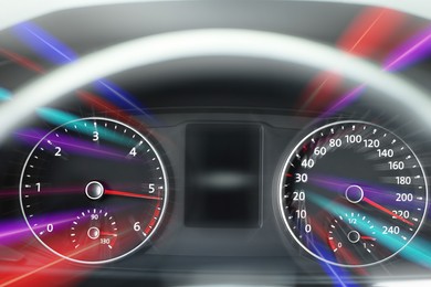 Image of Speedometer and tachometer behind steering wheel in car, motion blur effect