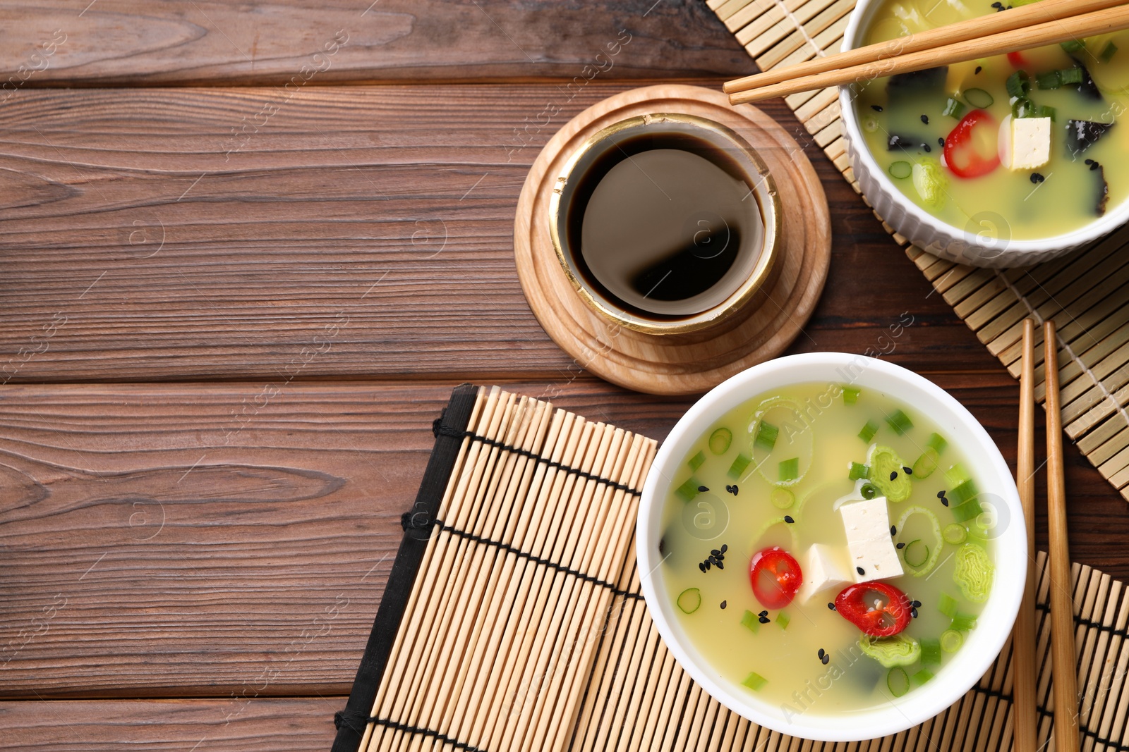 Photo of Bowls of delicious miso soup with tofu served on wooden table, flat lay. Space for text