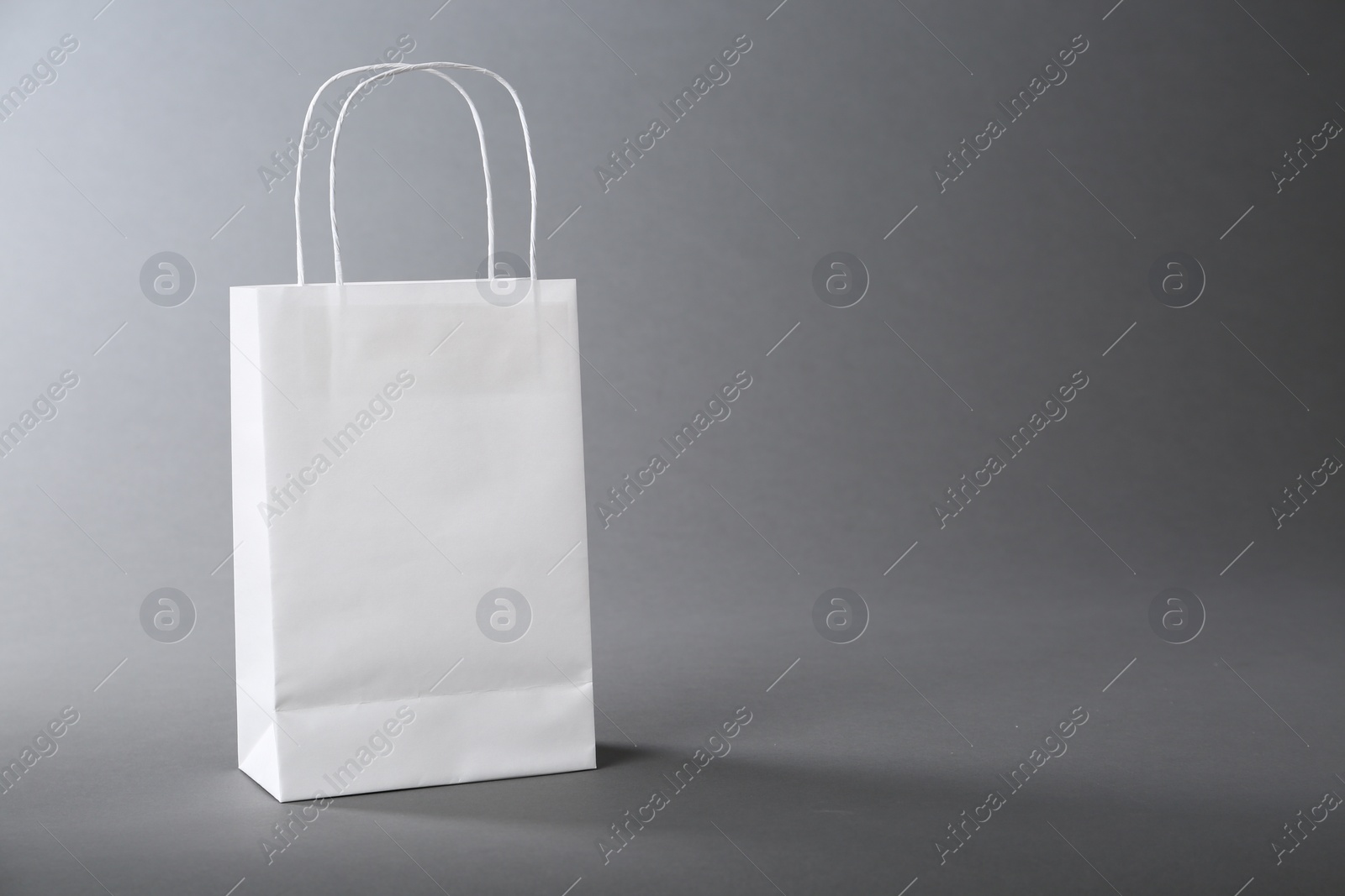 Photo of One white paper bag on grey background, space for text. Mockup for design