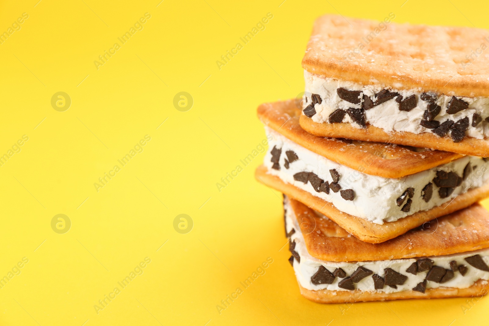 Photo of Sweet delicious ice cream cookie sandwiches on yellow background, closeup. Space for text