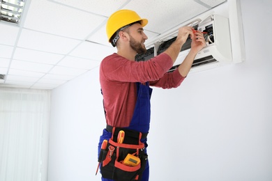 Photo of Electrician with screwdriver repairing air conditioner indoors