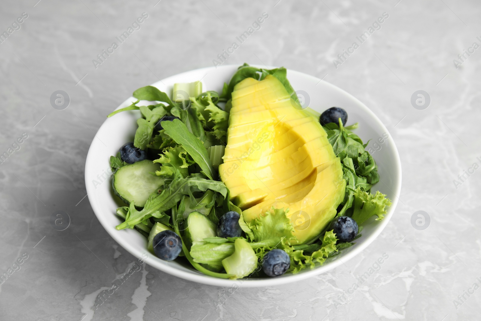 Photo of Delicious avocado salad with blueberries in bowl on grey marble table