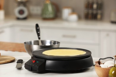 Cooking delicious crepe on electric pancake maker on white marble table in kitchen, space for text