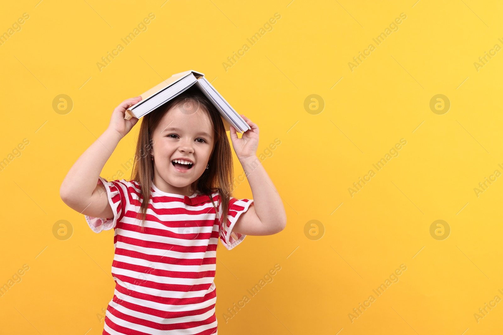 Photo of Cute little girl with open book on orange background. Space for text