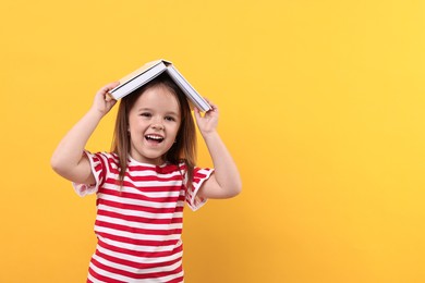 Photo of Cute little girl with open book on orange background. Space for text
