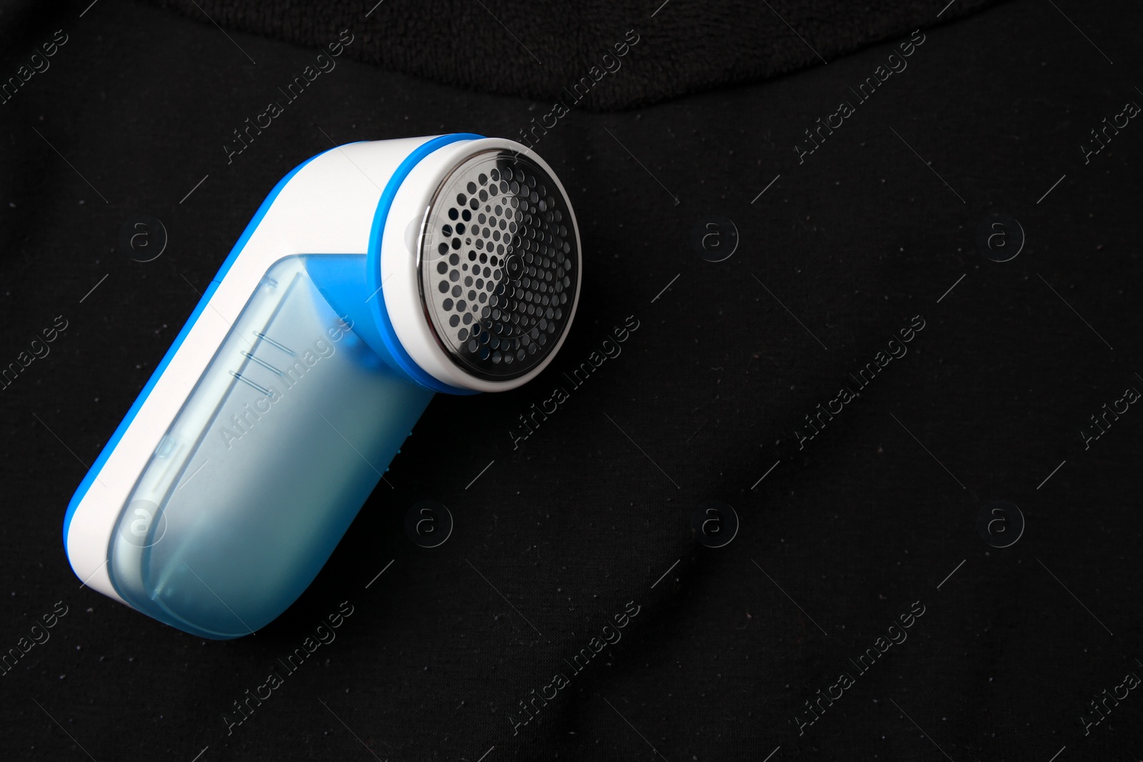 Photo of Modern fabric shaver on black cloth with lint. Space for text