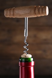 Opening wine bottle with corkscrew on dark brown background, closeup