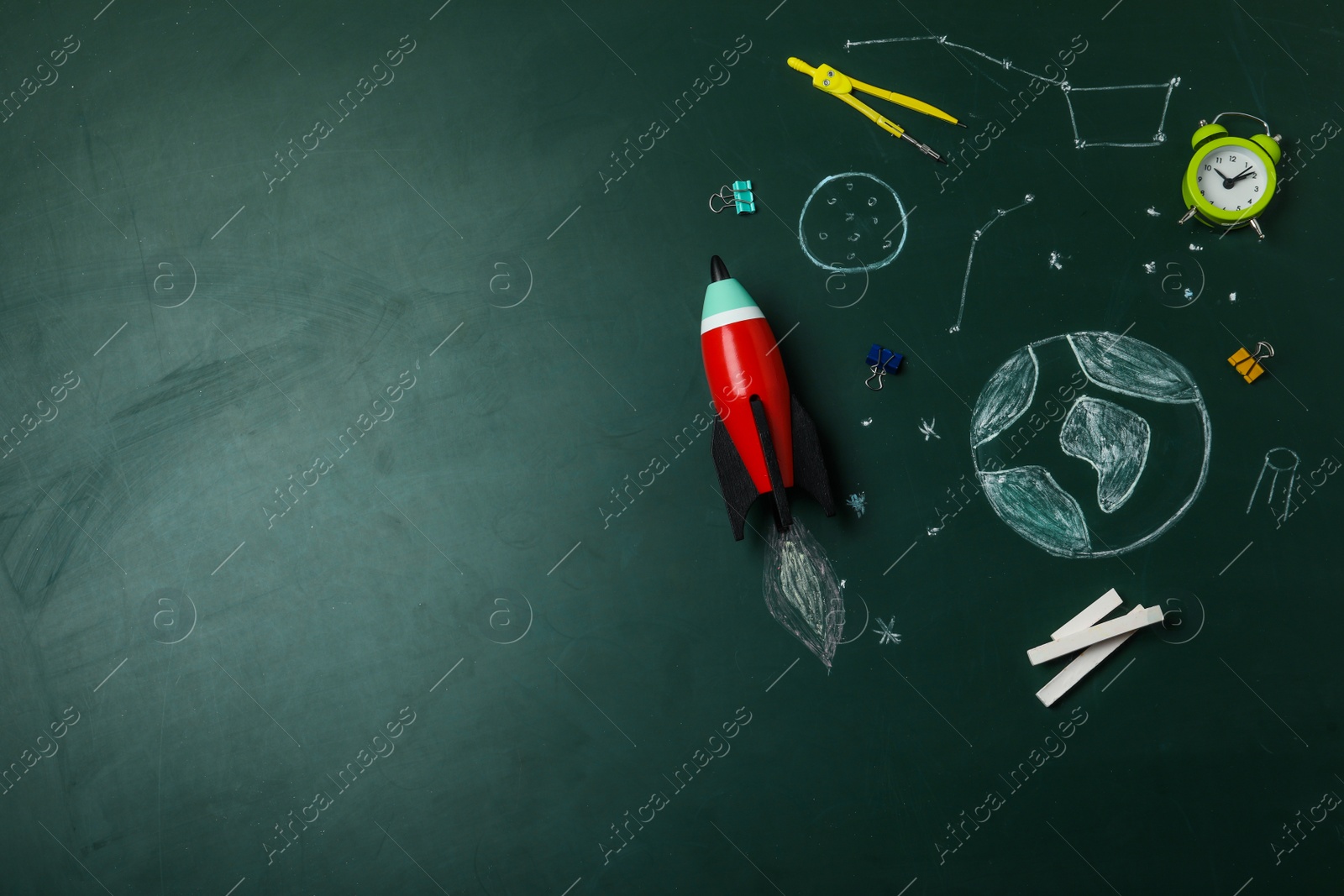 Photo of Bright toy rocket, school supplies and drawings on chalkboard, flat lay. Space for text