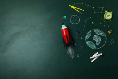 Photo of Bright toy rocket, school supplies and drawings on chalkboard, flat lay. Space for text