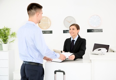 Photo of Young man filling form at reception desk in hotel