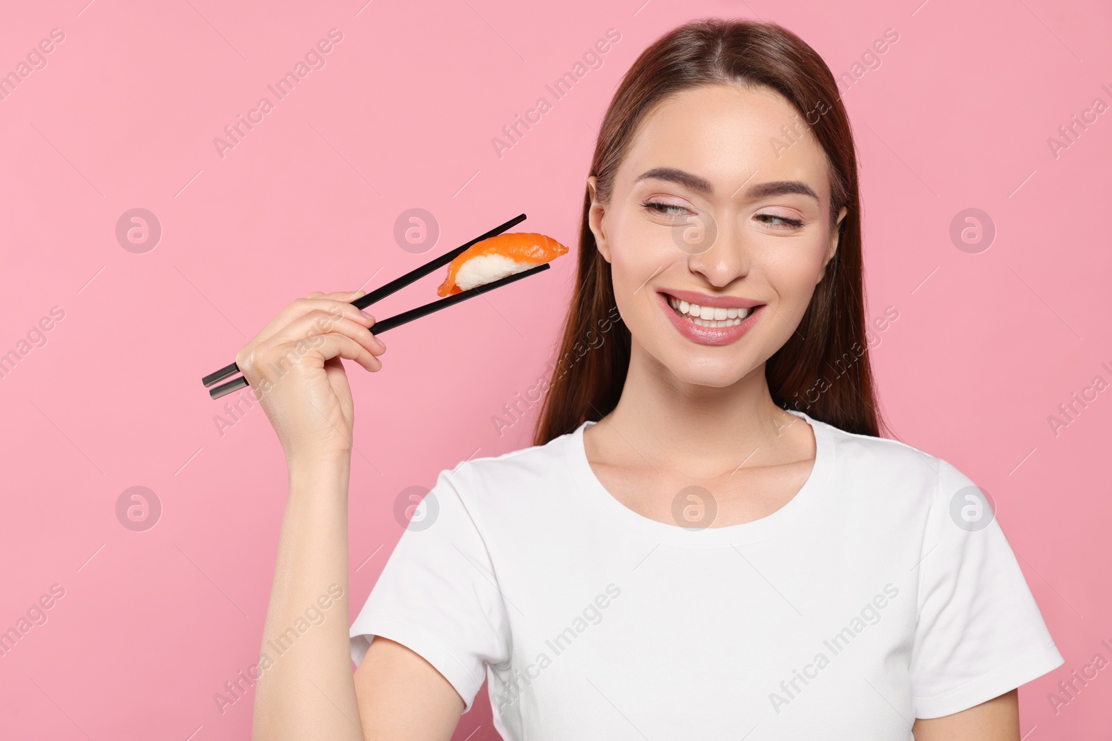 Photo of Beautiful young woman holding sushi with chopsticks on pink background