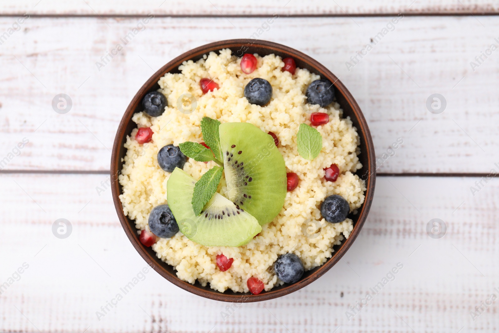Photo of Bowl of tasty couscous with kiwi, blueberries and pomegranate on white wooden table, top view