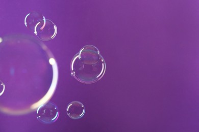 Beautiful transparent soap bubbles on violet background, space for text
