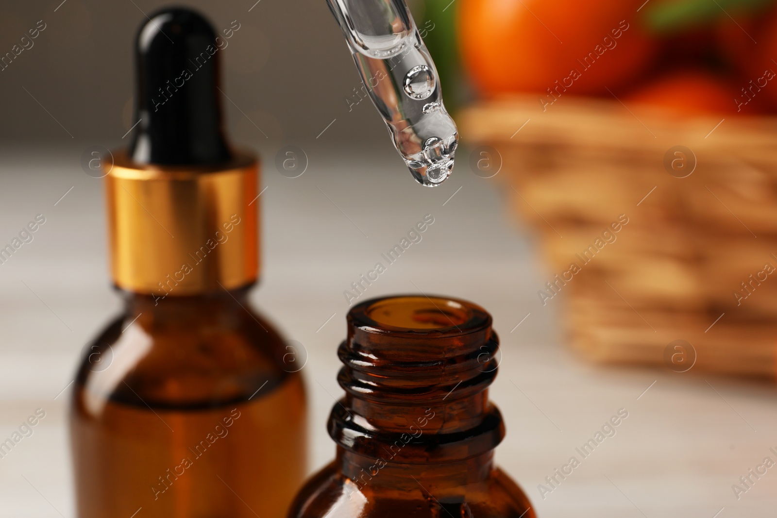 Photo of Tangerine essential oil dripping from pipette into bottle on blurred background, closeup
