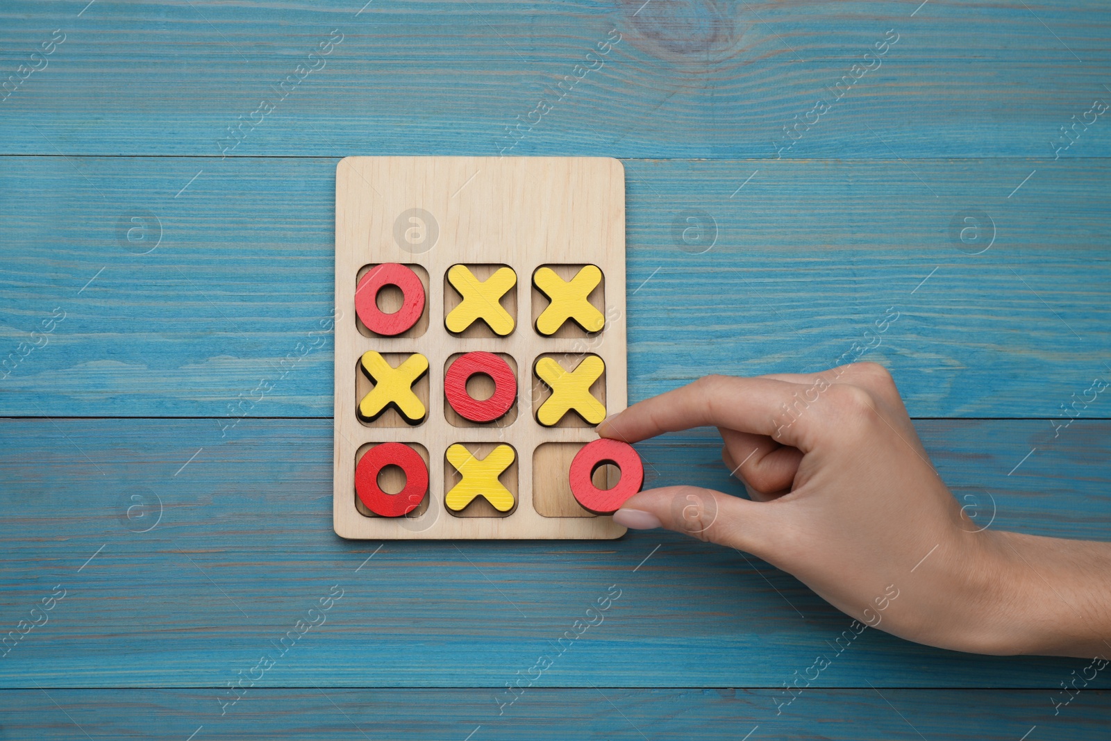 Photo of Woman playing tic tac toe game at light blue wooden table, top view