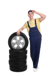 Male mechanic with car tires on white background