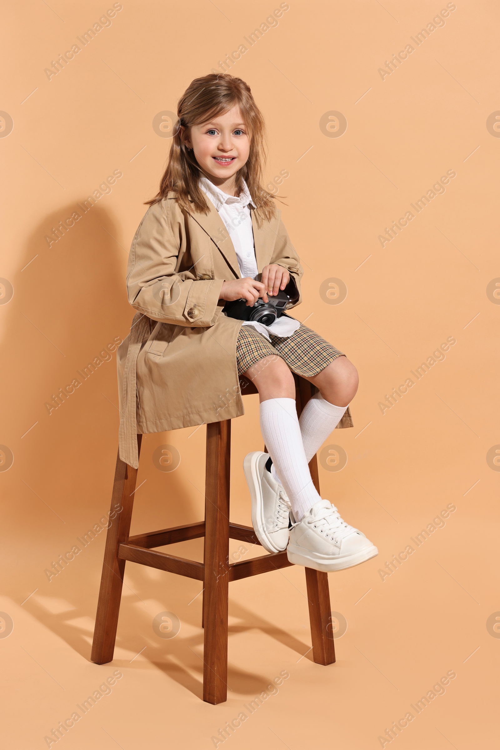 Photo of Fashion concept. Stylish girl with vintage camera on pale orange background