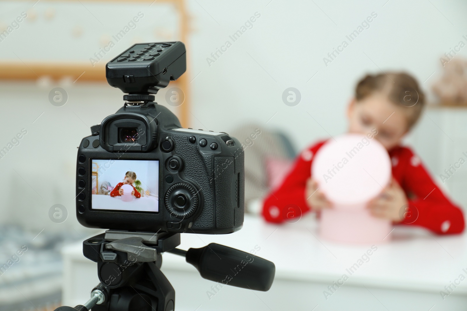 Photo of Cute little blogger with box recording video at home, focus on camera