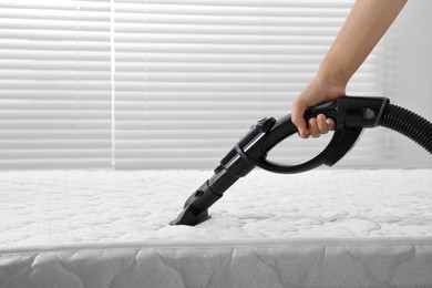 Photo of Woman disinfecting mattress with vacuum cleaner indoors, closeup. Space for text