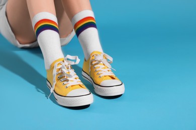 Photo of Woman wearing yellow classic old school sneakers on light blue background, closeup. Space for text