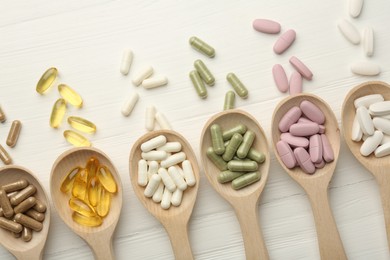 Different vitamin capsules in spoons on white wooden table, flat lay