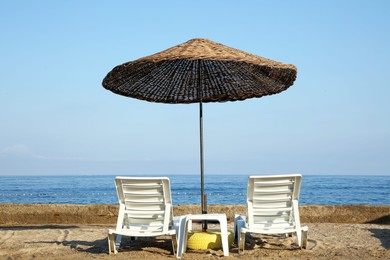 Photo of Two lounge chairs and beach umbrella on sea shore