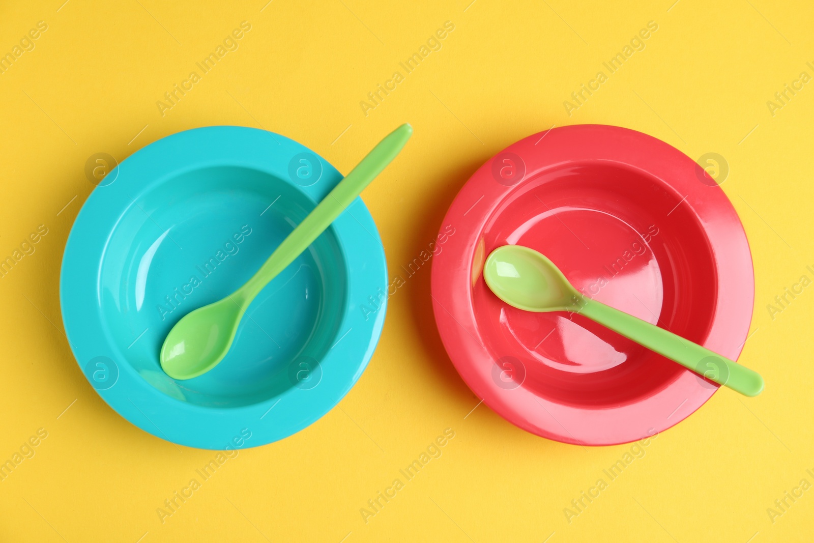 Photo of Set of colorful plastic dishware on yellow background, flat lay. Serving baby food