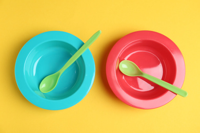 Set of colorful plastic dishware on yellow background, flat lay. Serving baby food