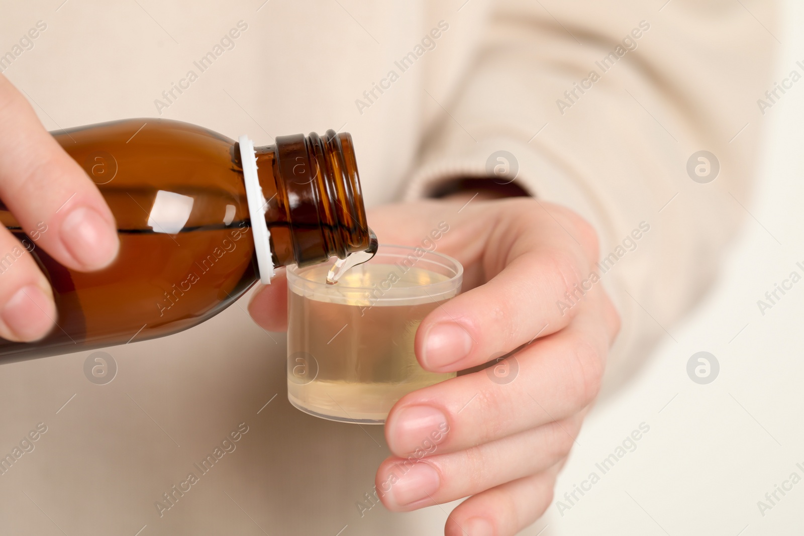 Photo of Woman pouring syrup from bottle into measuring cup, closeup. Cold medicine