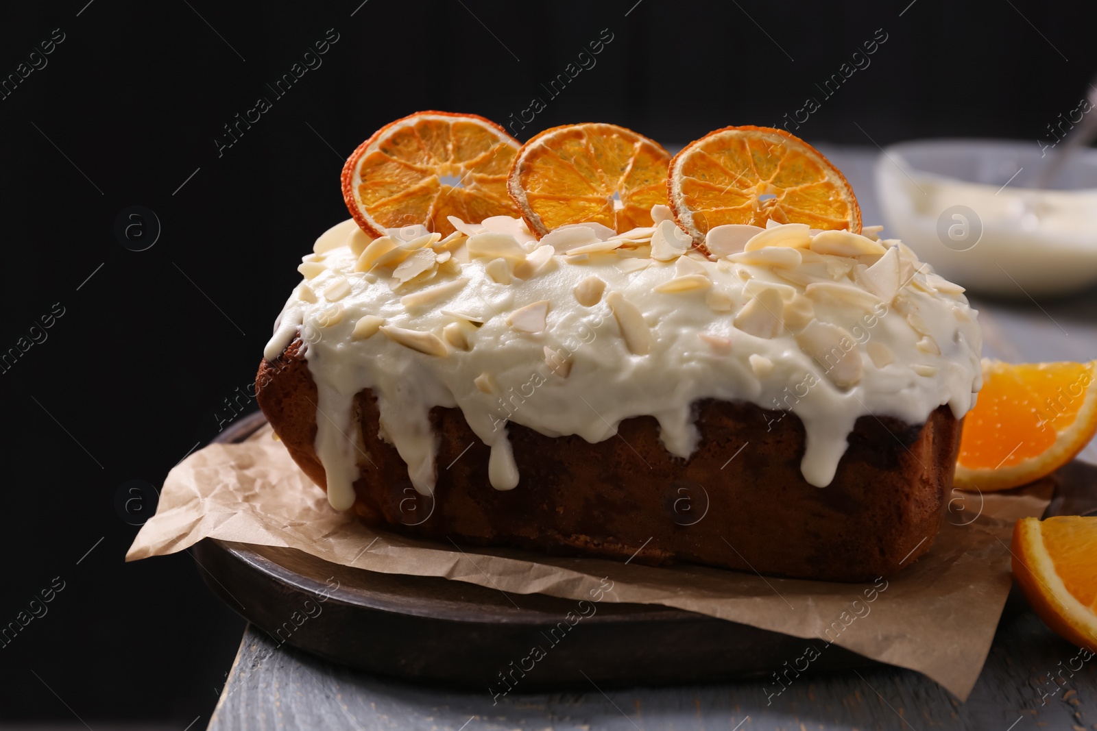 Photo of Delicious sweet cake with dry orange and almond petals on grey wooden table