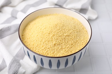 Raw couscous in bowl on white tiled table, closeup