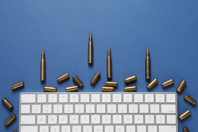 Photo of Bullets and computer keyboard on blue background, flat lay. Hybrid warfare concept