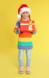 Photo of Cute little girl in Santa hat with Christmas gift on yellow background