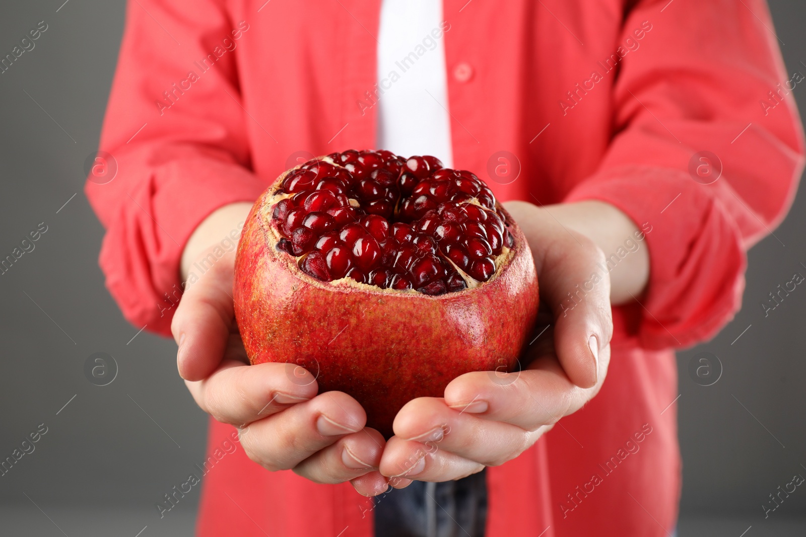 Photo of Woman holding fresh pomegranate on grey background, closeup