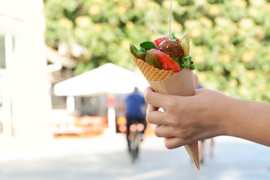 Photo of Woman holding wafer with falafel and vegetables outdoors, closeup. Space for text