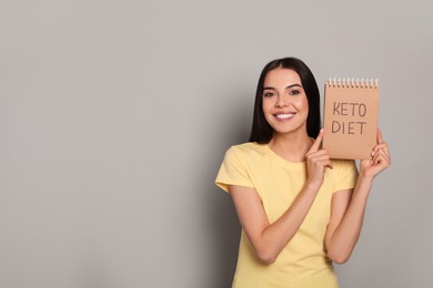 Happy woman holding notebook with words Keto Diet on light grey background. Space for text