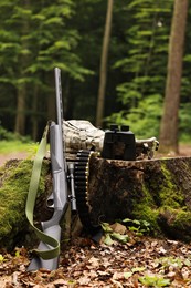 Hunting rifle, backpack, cartridges and binoculars on tree stump in forest