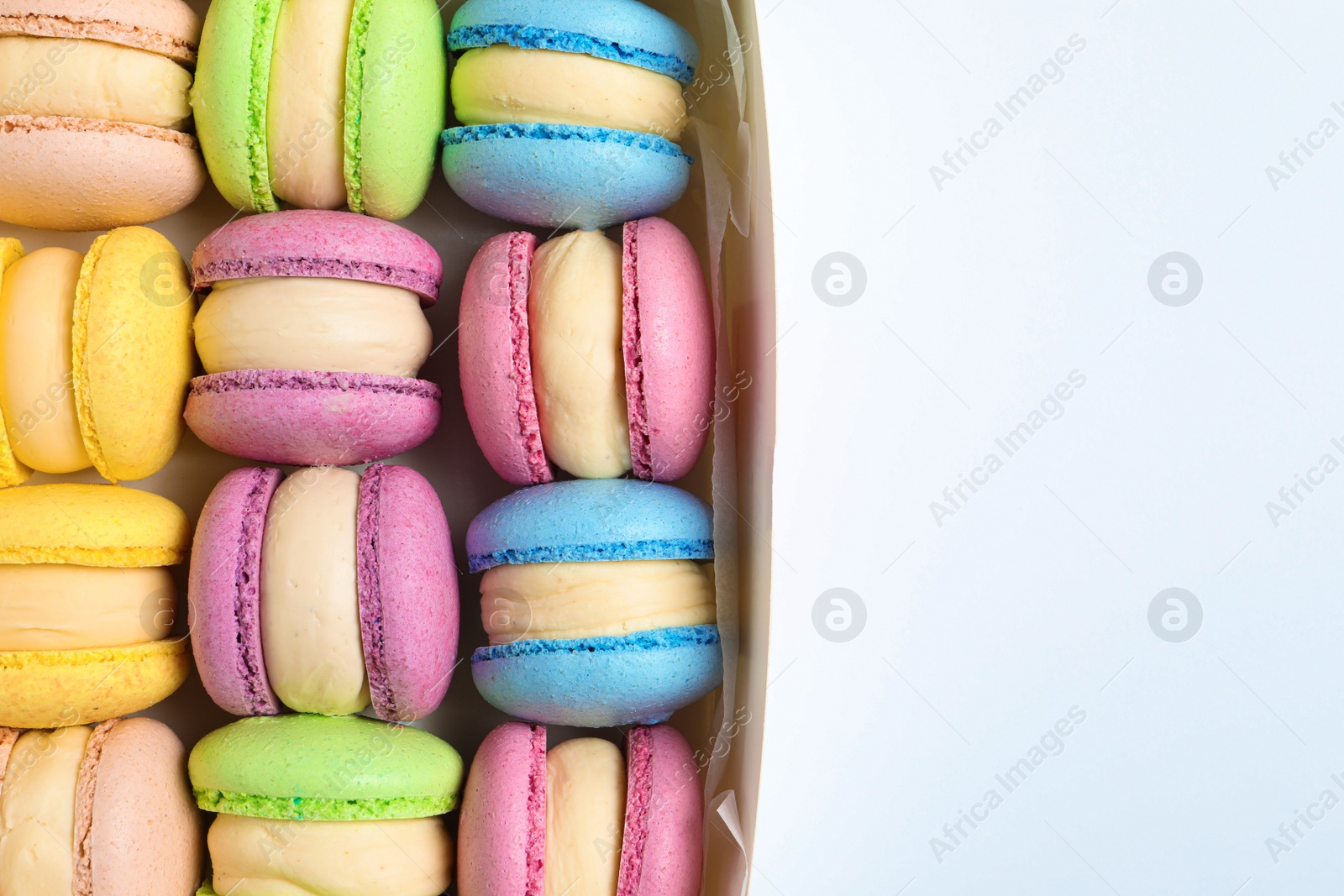 Photo of Many delicious colorful macarons in box on white background, top view