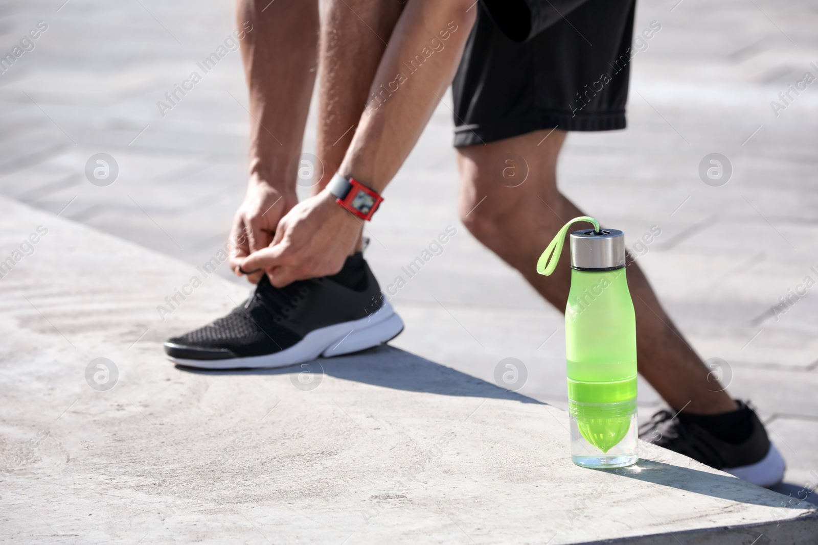 Photo of Sporty man tying shoelaces near bottle of water outdoors on sunny day