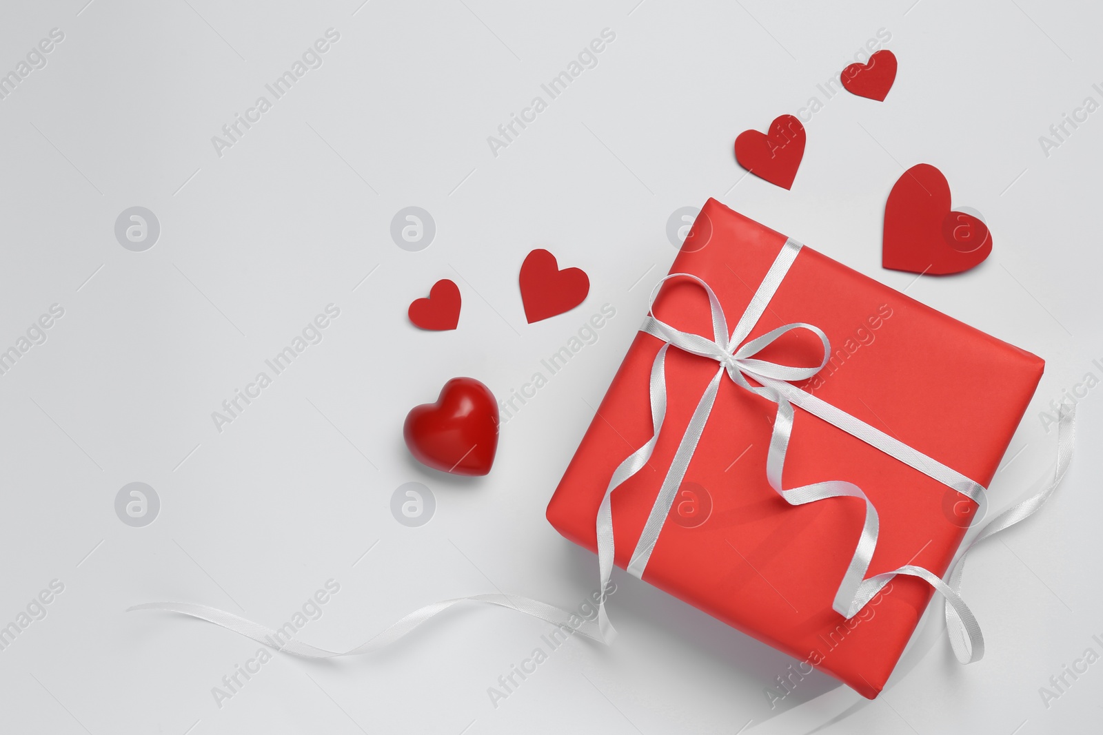 Photo of Gift box with bow and decorative red hearts on white background, top view