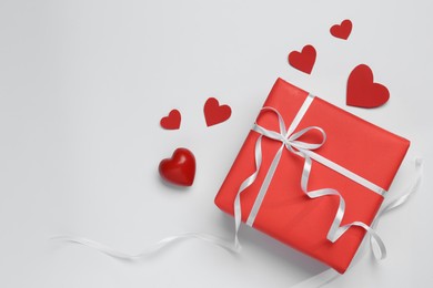 Gift box with bow and decorative red hearts on white background, top view