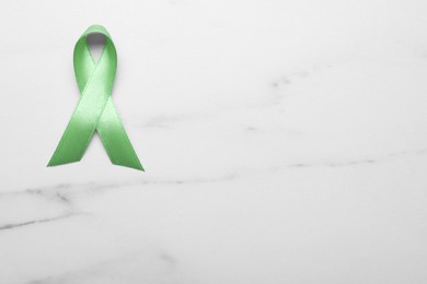 Photo of World Mental Health Day. Green ribbon on white marble table, top view with space for text