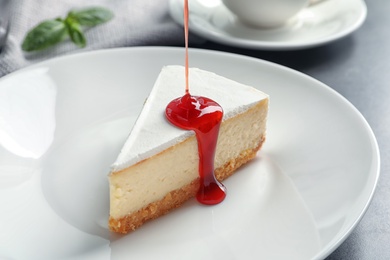 Photo of Pouring sweet jam onto delicious cheesecake served on plate