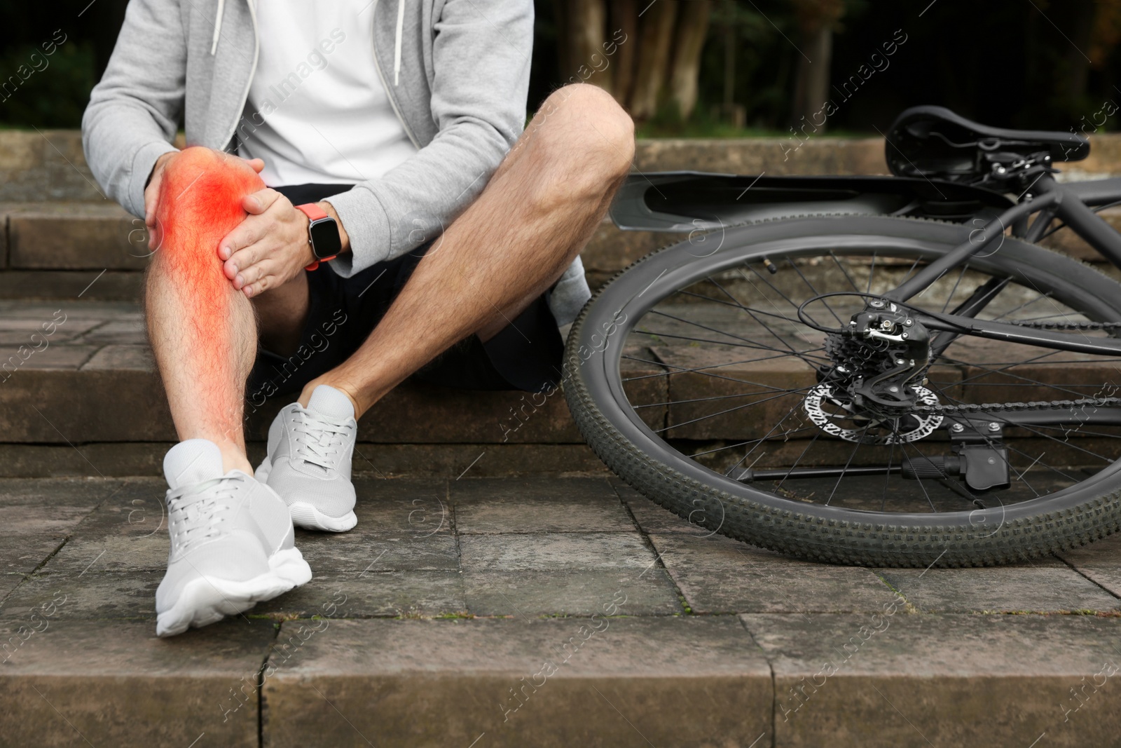 Image of Man with injured knee on steps near bicycle outdoors, closeup