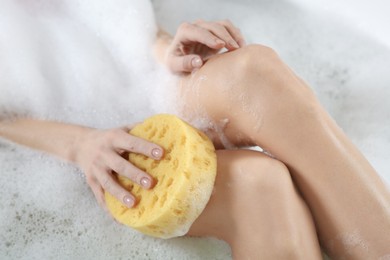 Photo of Woman rubbing her leg with sponge while taking bath, closeup