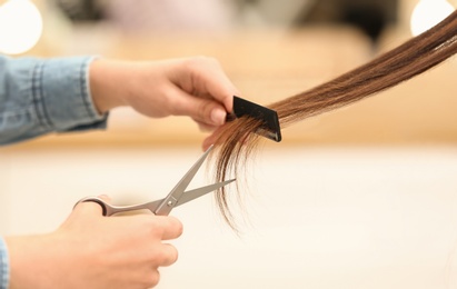 Barber making stylish haircut with professional scissors in beauty salon, closeup