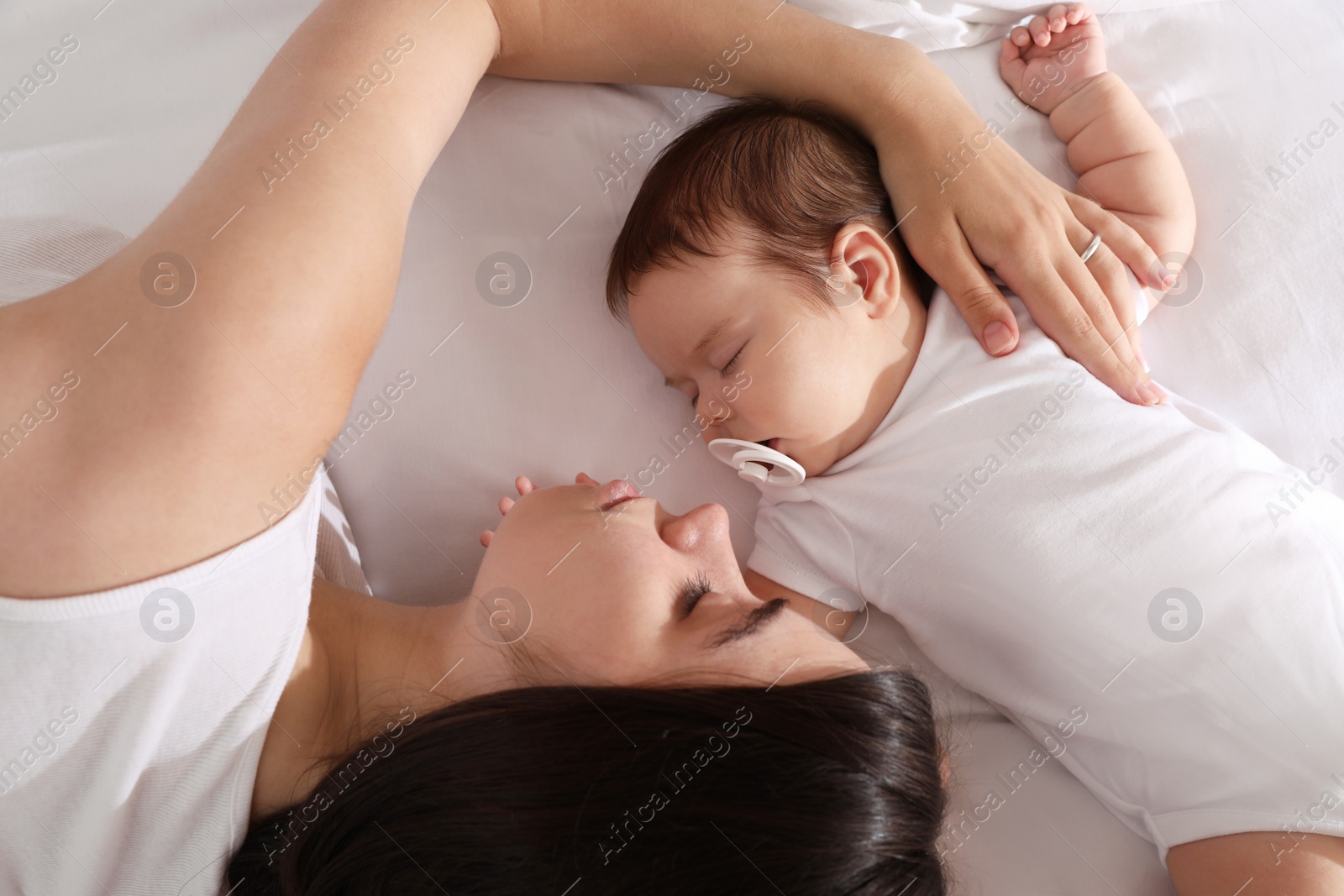 Photo of Young mother resting near her sleeping baby on bed, top view